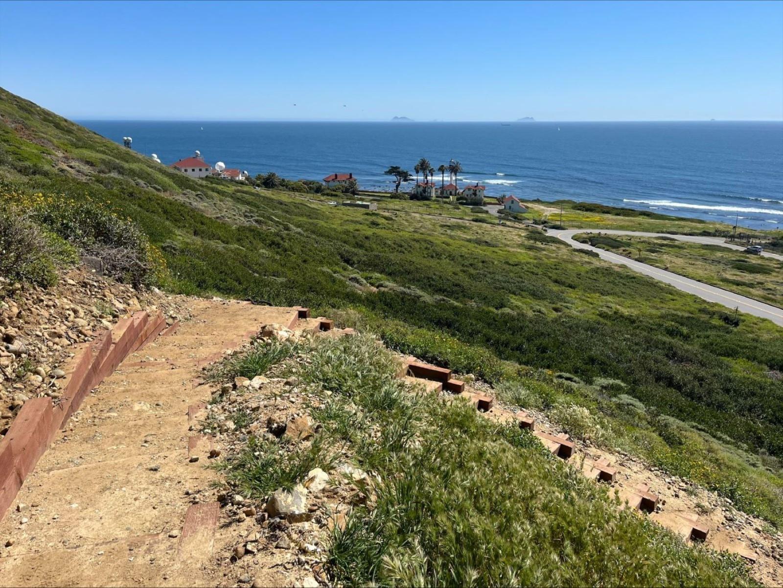 A windy dirt path on a hillside overlooking the ocean.