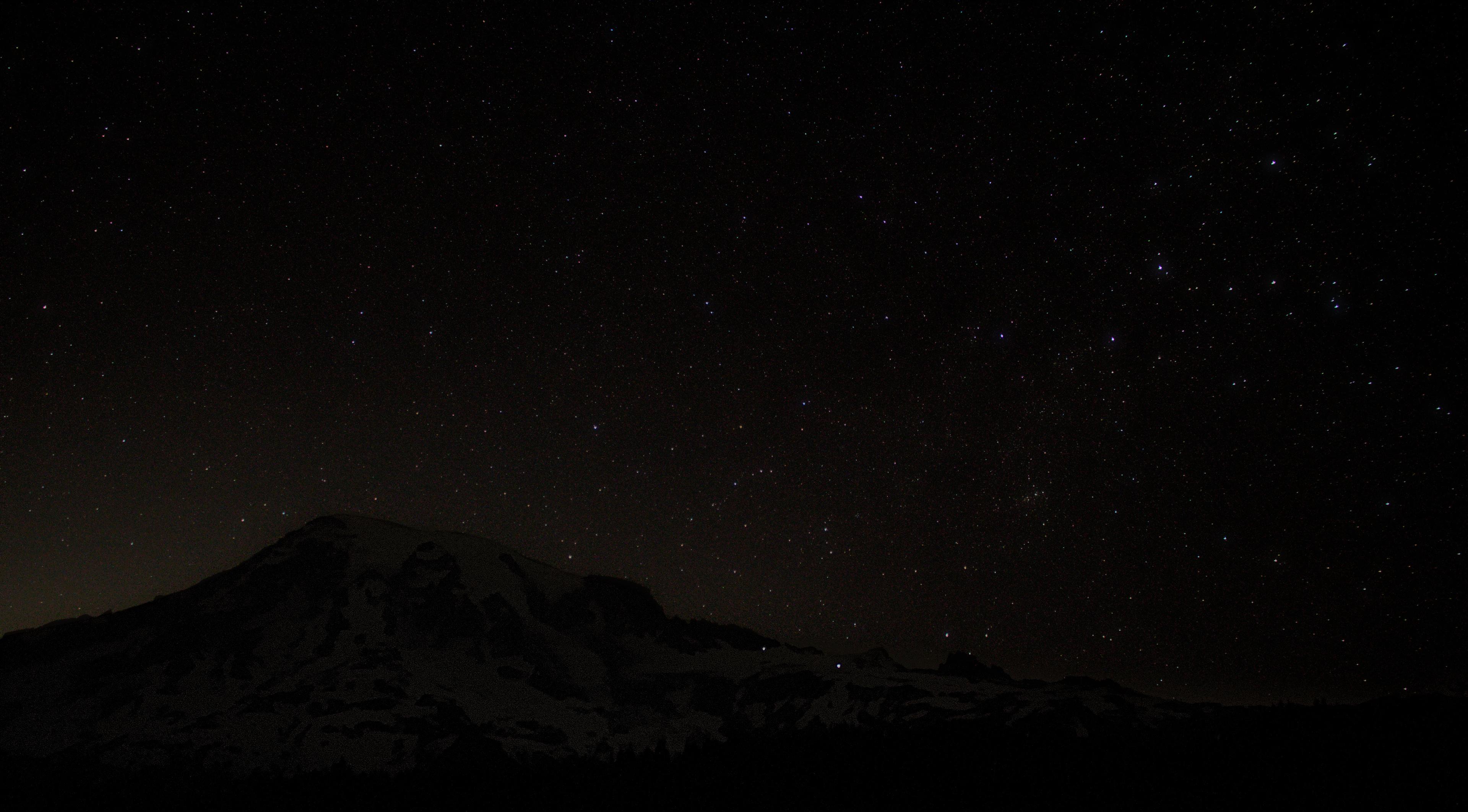A starry sky stretches above a large volcanic peak.
