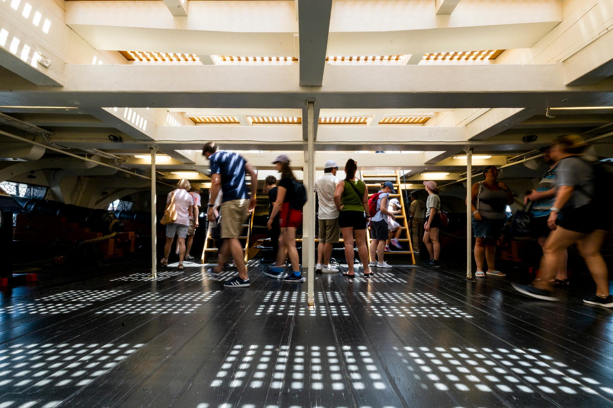 below deck of the frigate USS Constitution. A shadowed and short deck with people walking around.