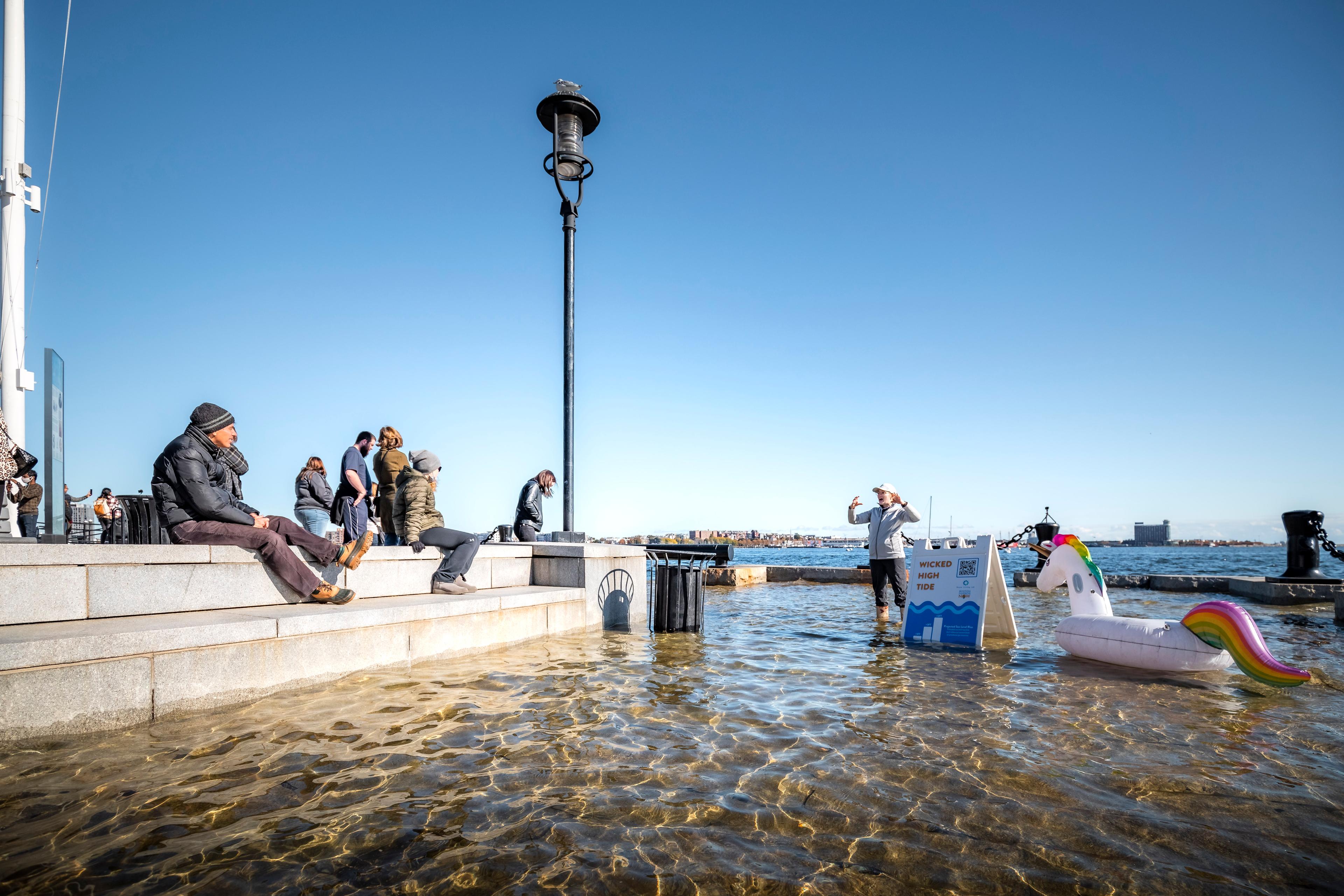 People sitting on Long Wharf as someone in wellies stands in the flooded lower area of the walkway.