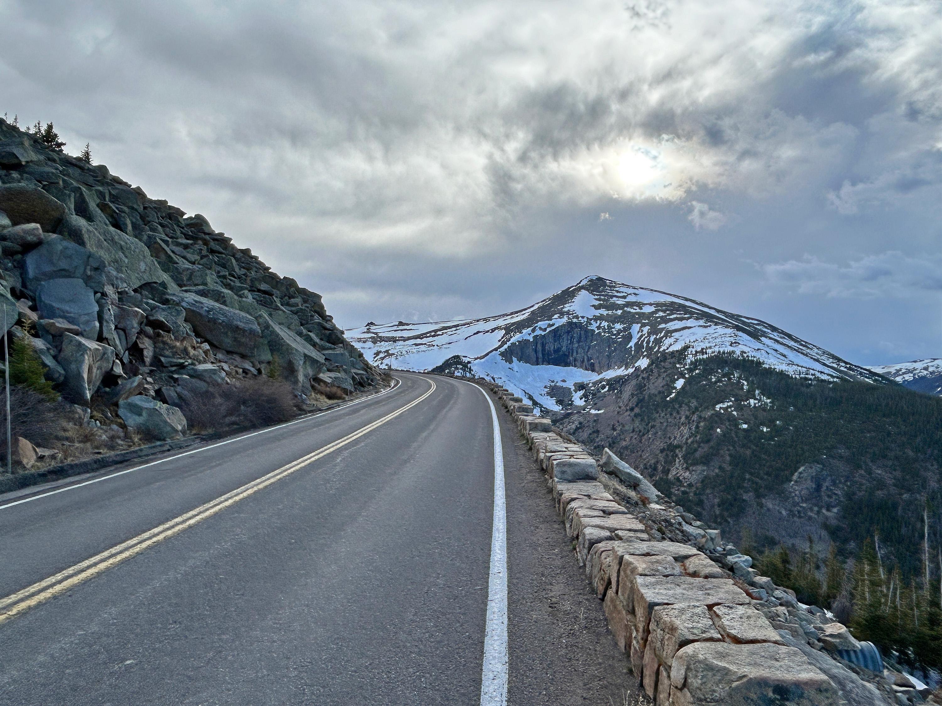 View of mountains off to the distance with a steep drop off beyond a rock-lined wall to the right