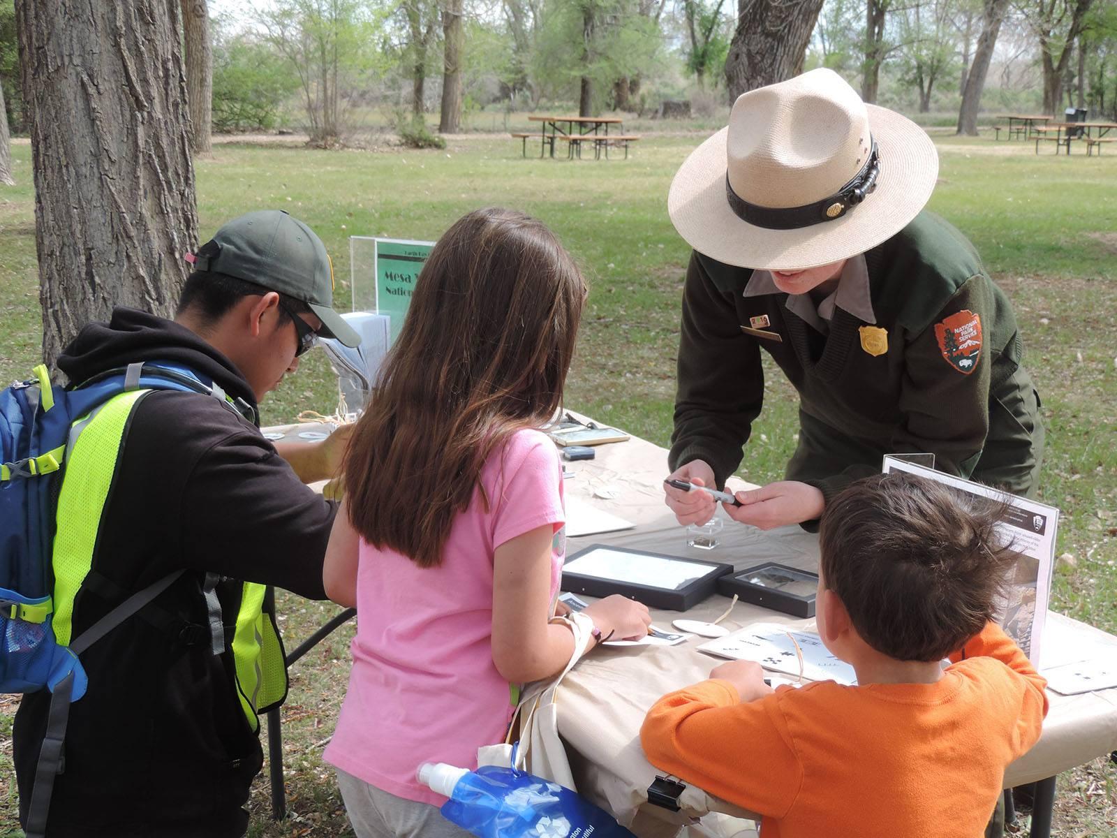 3 children work at a table in front of a park ranger.