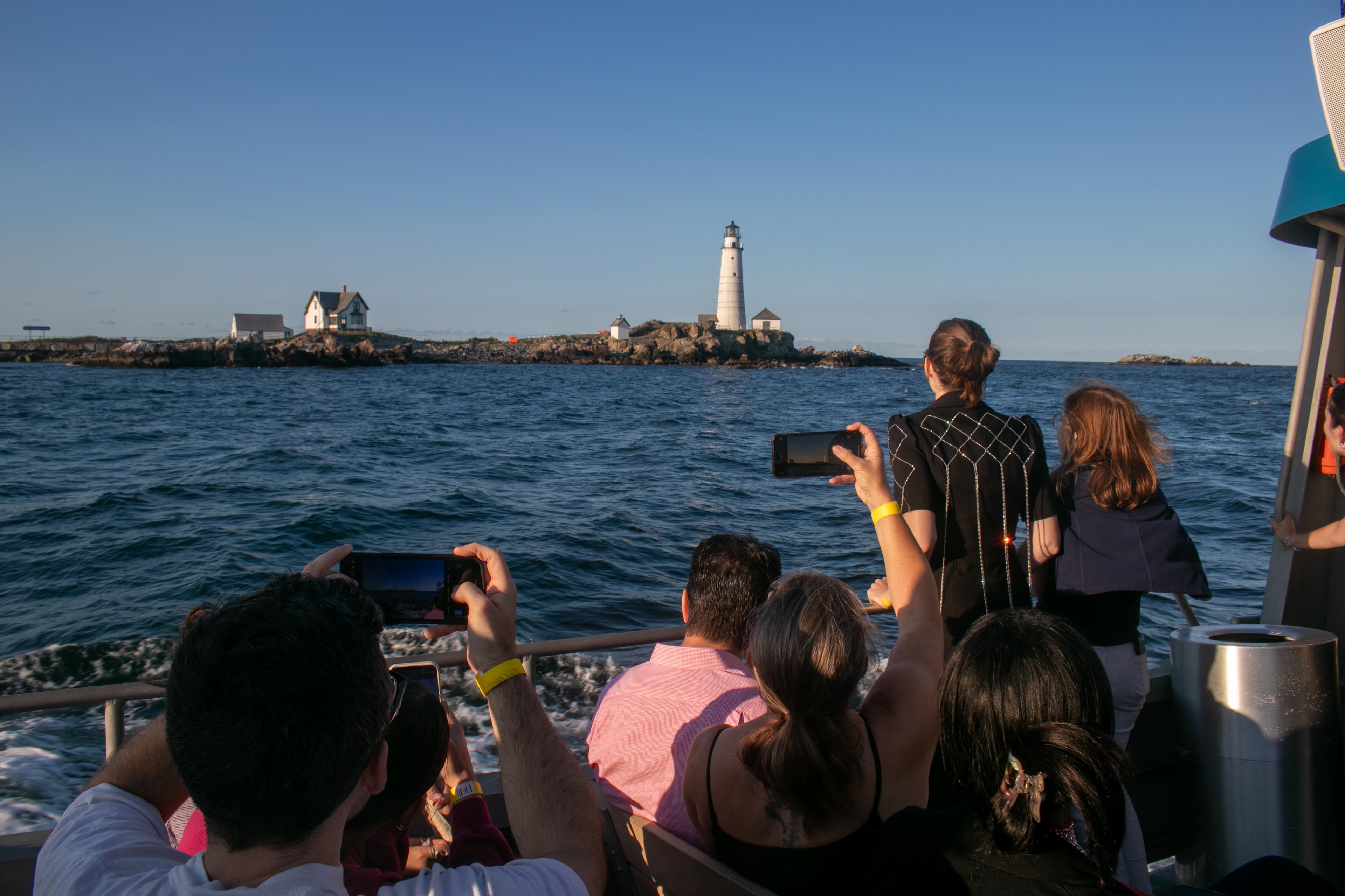 People on a boat taking pictures or looking at a white lighthouse on a rocky island.