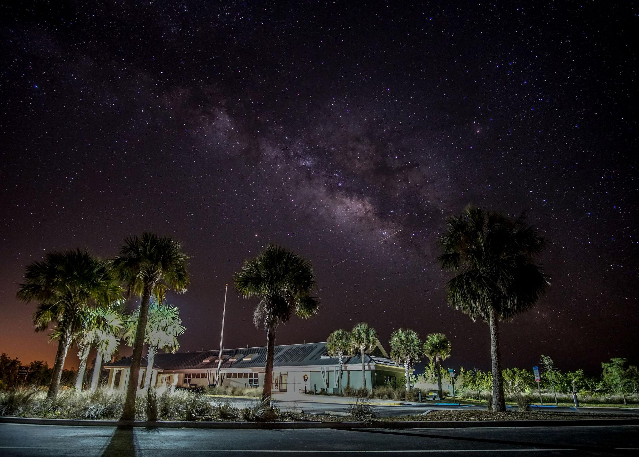 Visitor Center illuminated at night with night sky visible and palm trees in the foreground
