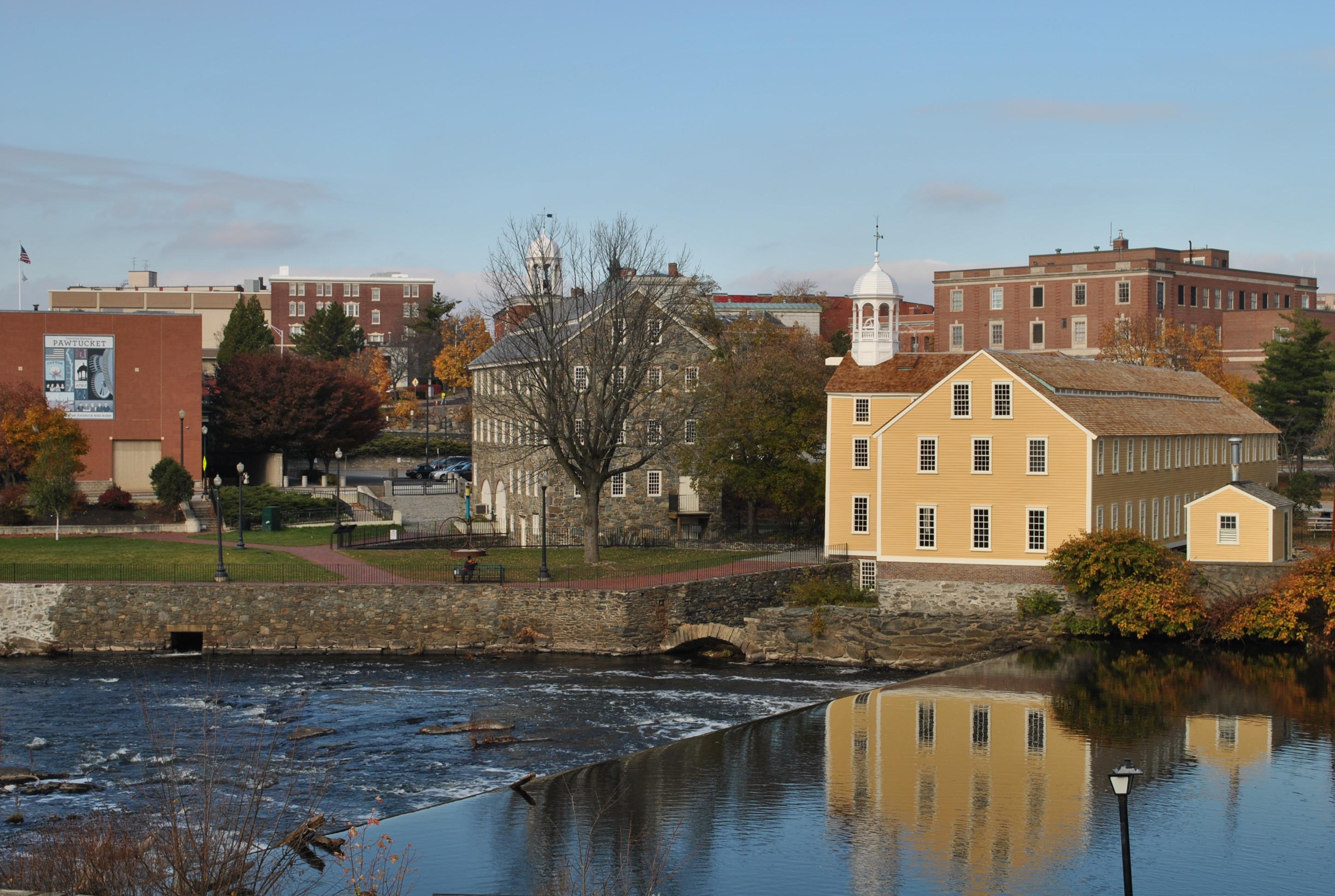 River in foreground with yellow mill and other buildings in distance