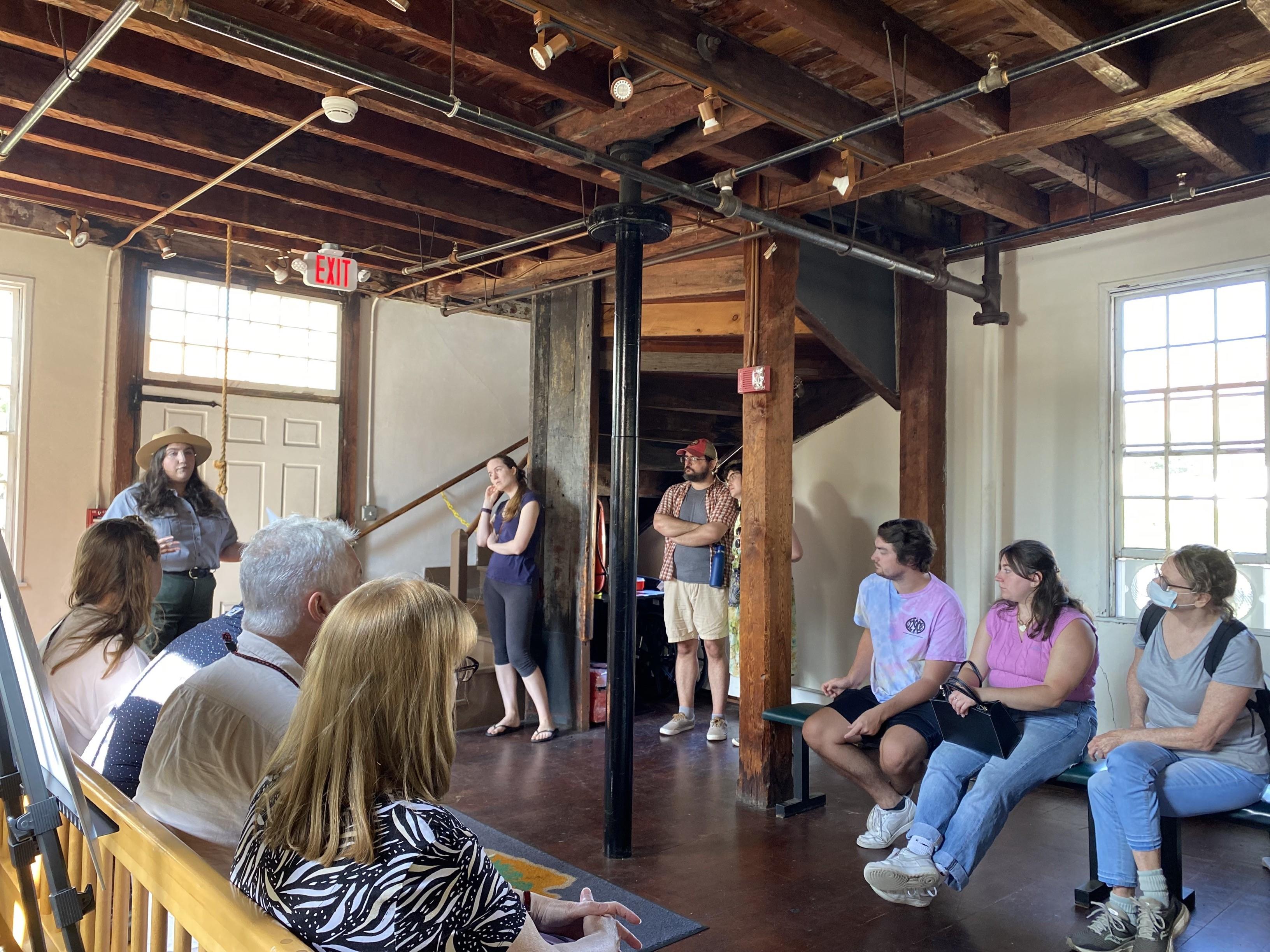 Group of visitors sitting and standing while listening to Park Ranger inside of wood framed building